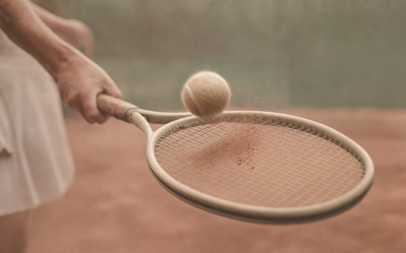Offenes Schlägerblatt schneidet durch einen Tennisball, weiches pastellfarbenes Licht